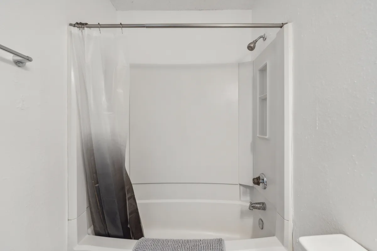 A stylish and sparkling clean bathroom is shown, with a sleek bathtub, fresh shower curtain, and modern shower head. The space is bright and tidy, exuding a calming ambiance ideal for a refreshing morning routine or unwinding after a busy day.