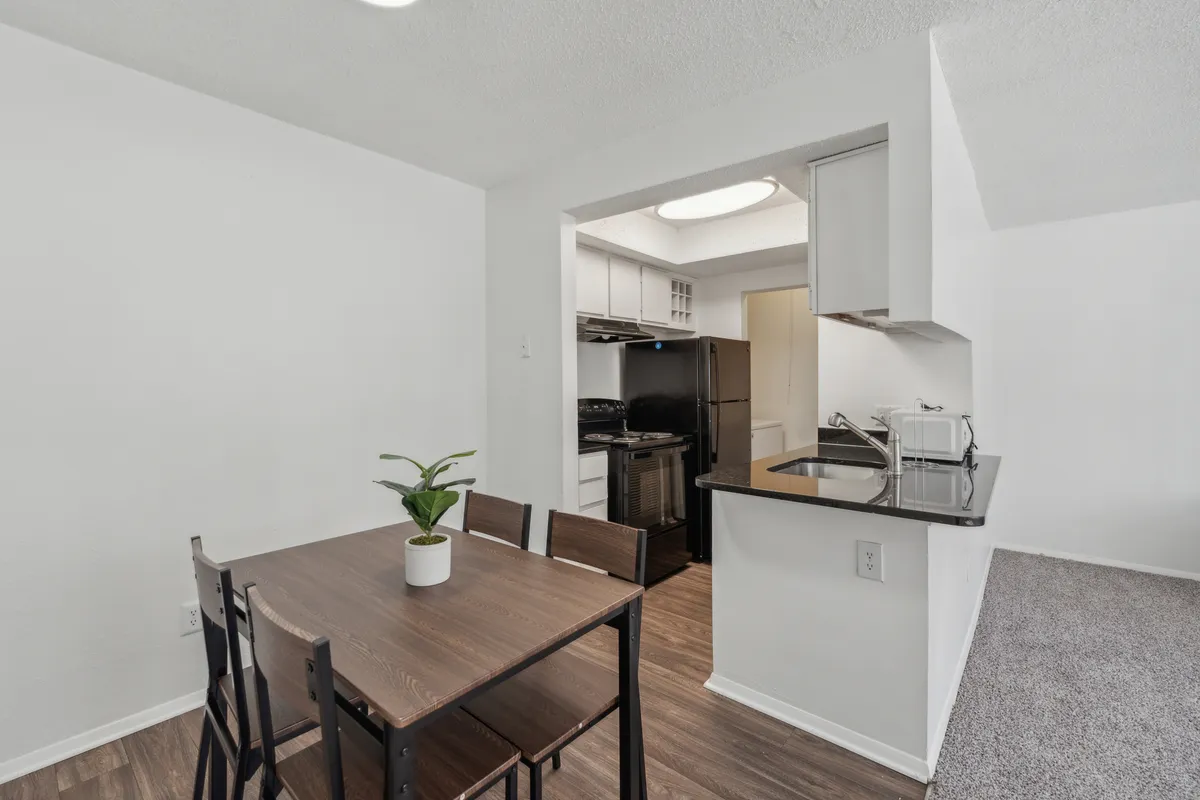 A cozy dining area seamlessly integrated with the kitchen, featuring a stylish dining table, kitchen zone, and a potted plant that adds a touch of natural warmth. The scene suggests shared meals, casual gatherings, and culinary enjoyment.