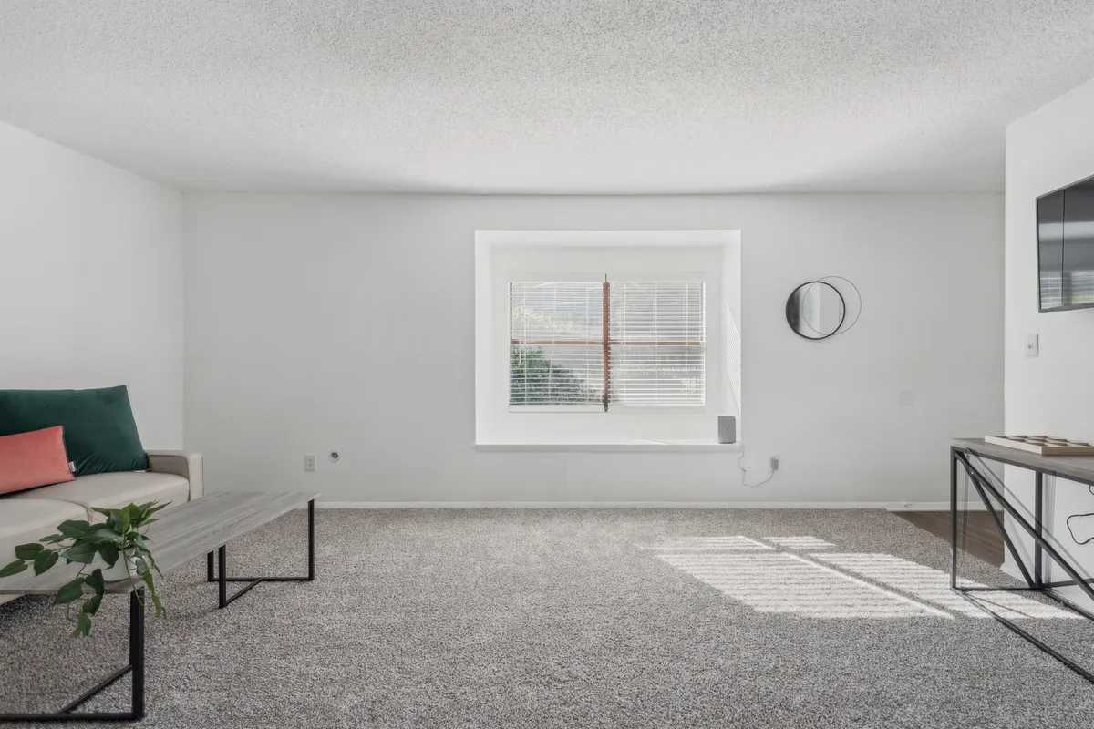 A calm and open living area with large windows, a streamlined sofa, a minimalist coffee table, and a decorative mirror. The space is bright and airy, suggesting both relaxation and a welcoming entry point.